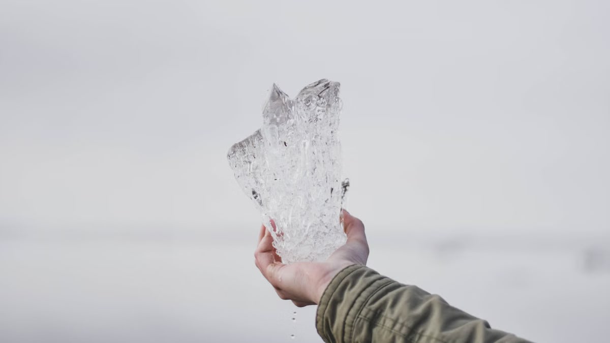 A hand holding a large piece of clear ice against a light background.